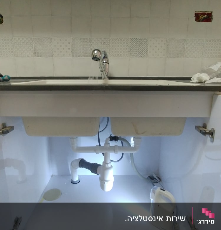 כיור מטבח עם צנרת ותאורה מתחת לארון
